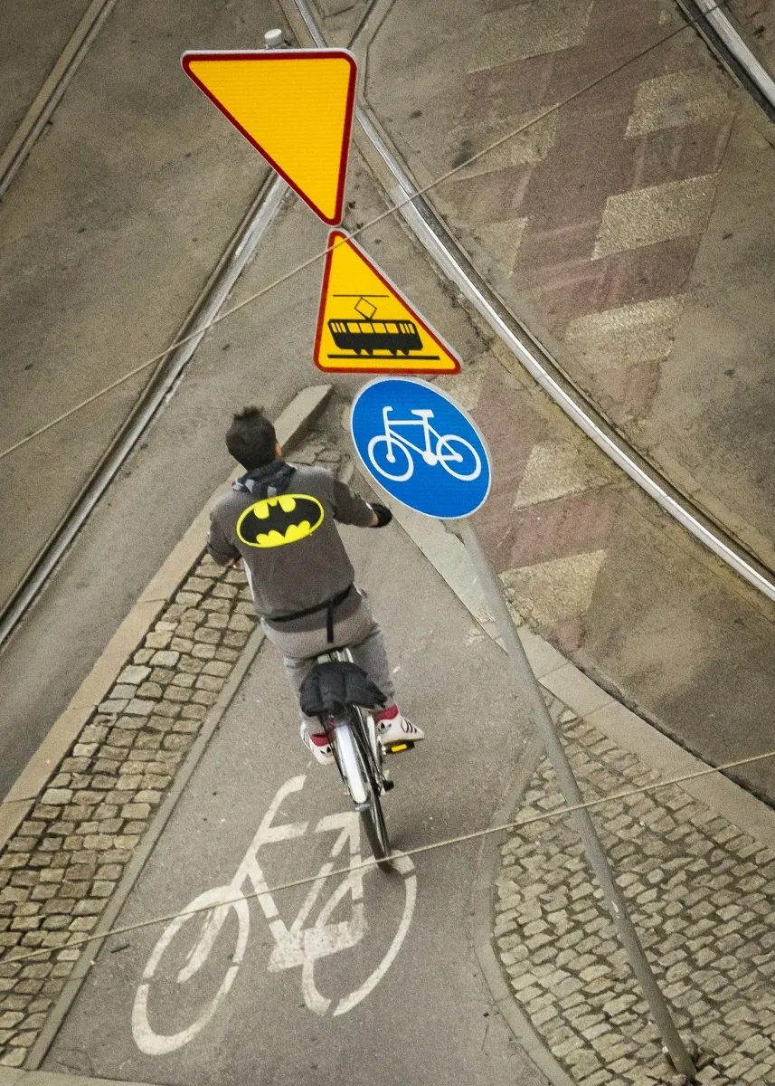 Cyclist in a Batman sweatshirt riding through a marked bike lane beneath traffic signs